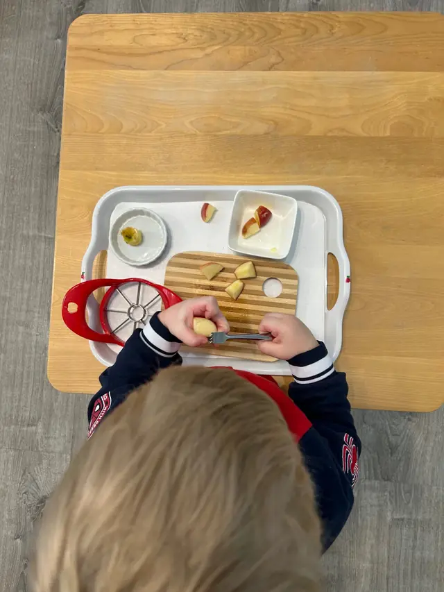 Child preparing fruit at a Montessori practical life table